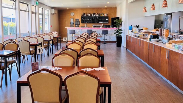 A spacious dining area with multiple tables and chairs, a bar counter with a variety of items, and a large window providing natural light. - Airport Gateway Hotel (Auckland)