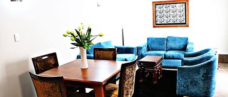 A dining area with a wooden table and chairs, a vase with flowers, and a blue sofa set.