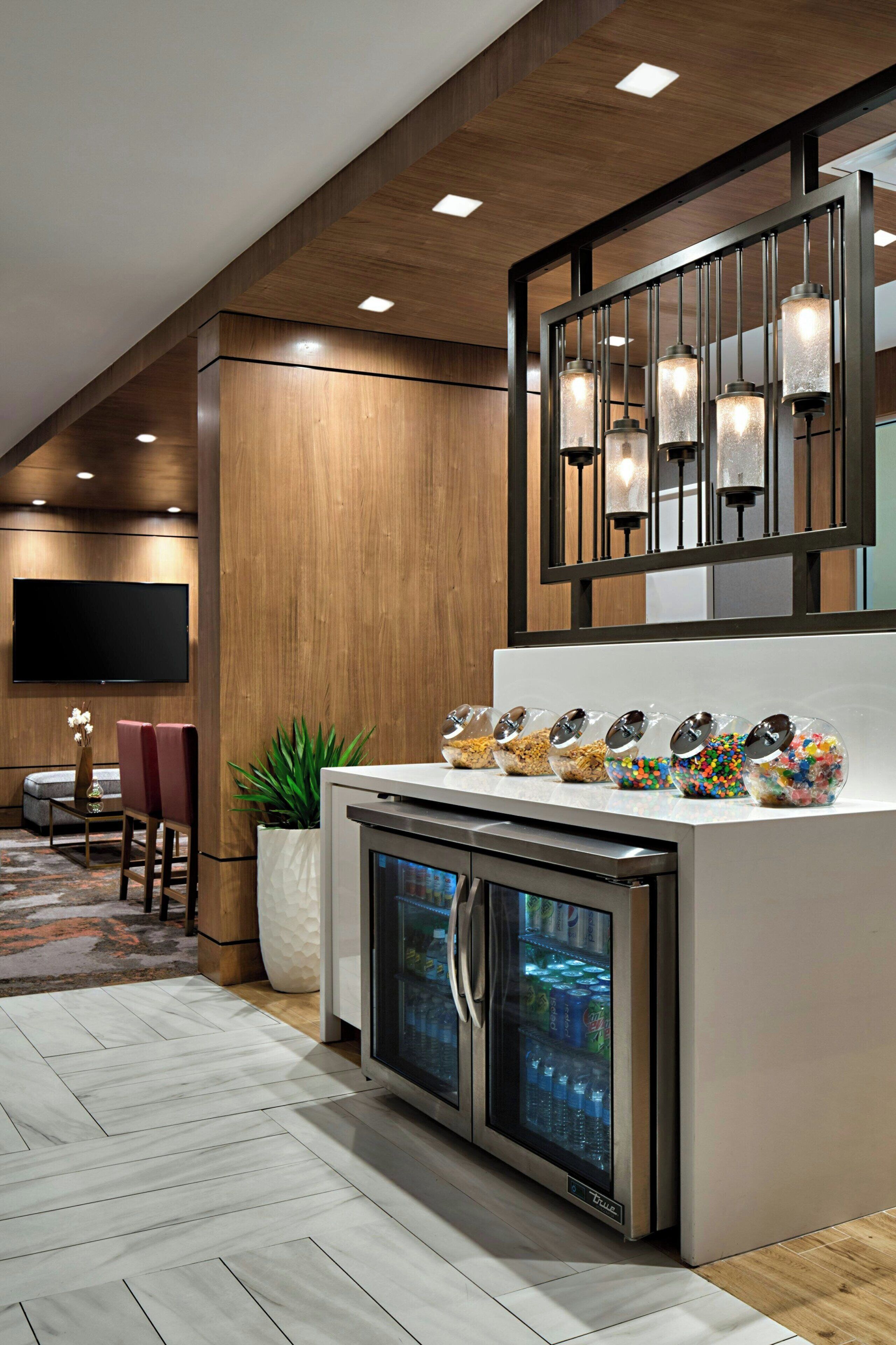 Un bar d’hôtel moderne doté d’un plafond en bois, d’un téléviseur à écran plat et d’un réfrigérateur à porte vitrée.