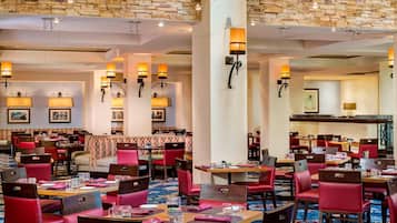 A hotel dining area with multiple tables and chairs, stone wall decor, and wall-mounted lighting.