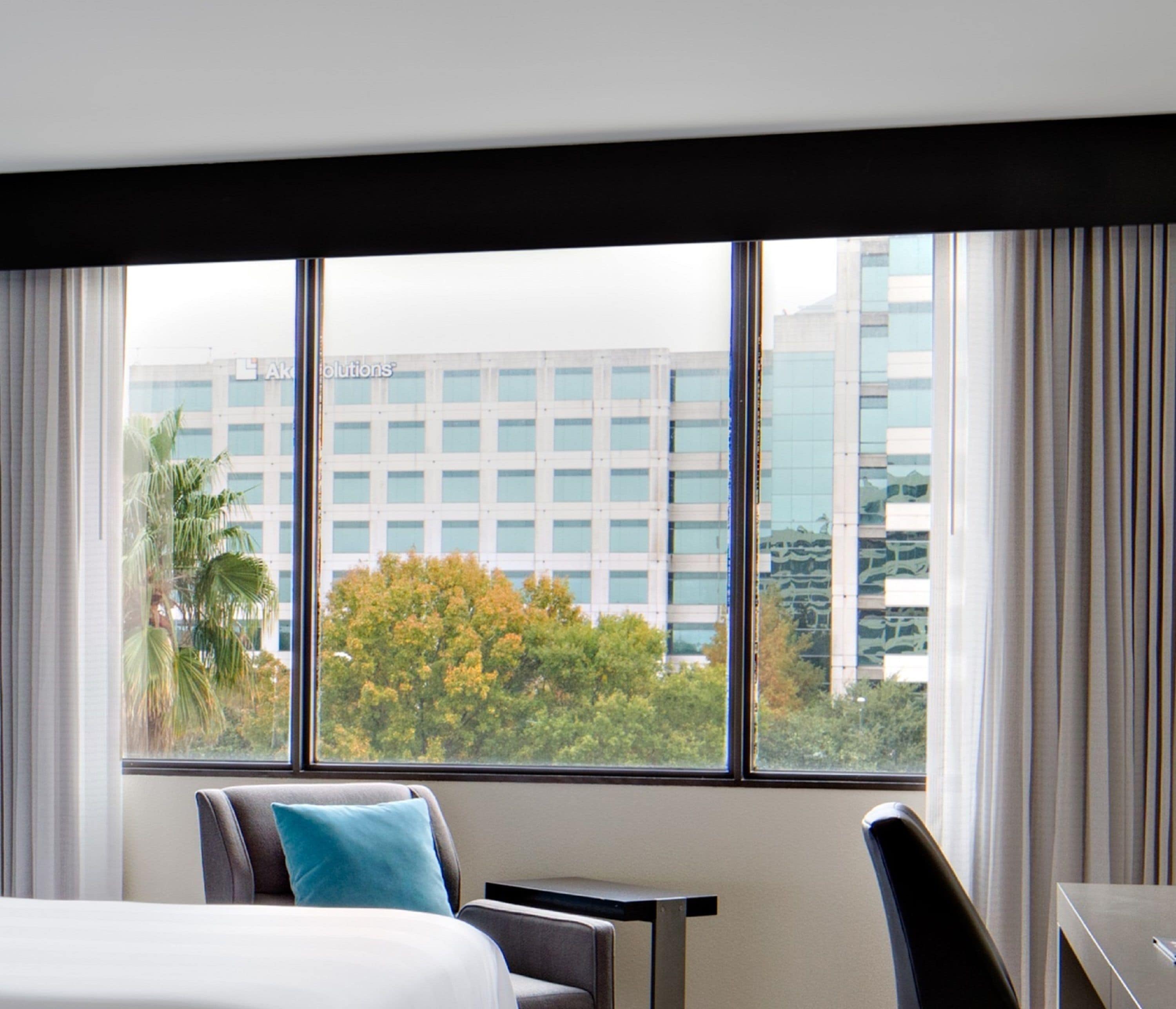 Ein Hotelzimmer mit großem Fenster, einem Bett, einem Schreibtisch und einem Sessel.