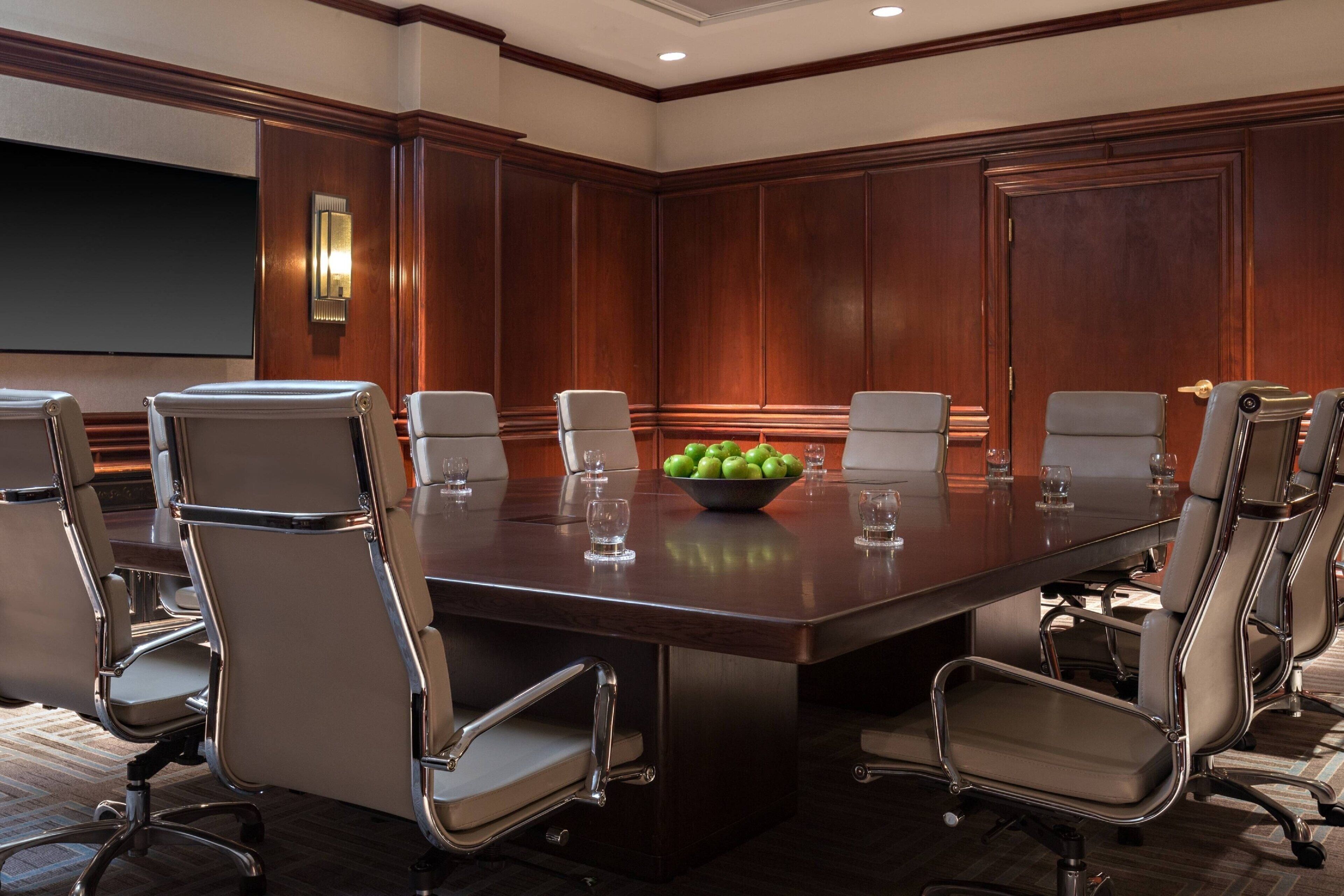 A conference room with a large table, eight chairs, a projector screen, and a bowl of apples.