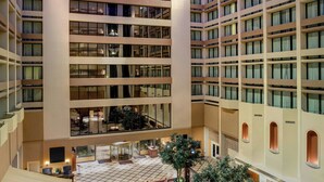 A spacious atrium with multiple floors, a central seating area with sofas and chairs, and a large tree.