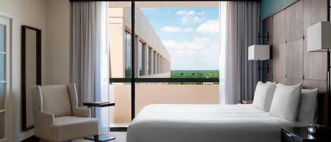 Habitación de hotel con una cama grande, una silla, una mesita de noche y vistas al exterior.