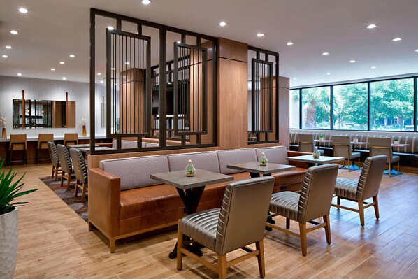 Un restaurant moderne doté d’un plancher en bois, de sièges confortables et de grandes fenêtres donnant sur un paysage verdoyant.