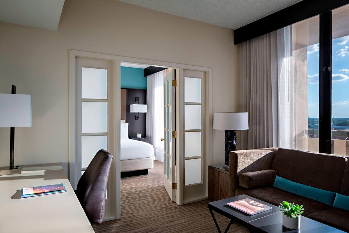 A hotel room with a bed, a desk, a sofa, and a large window with a view.