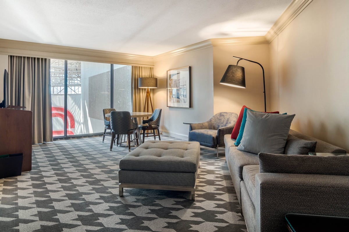 A hotel room with a patterned carpet, a sofa, a chair, a table, and a lamp.