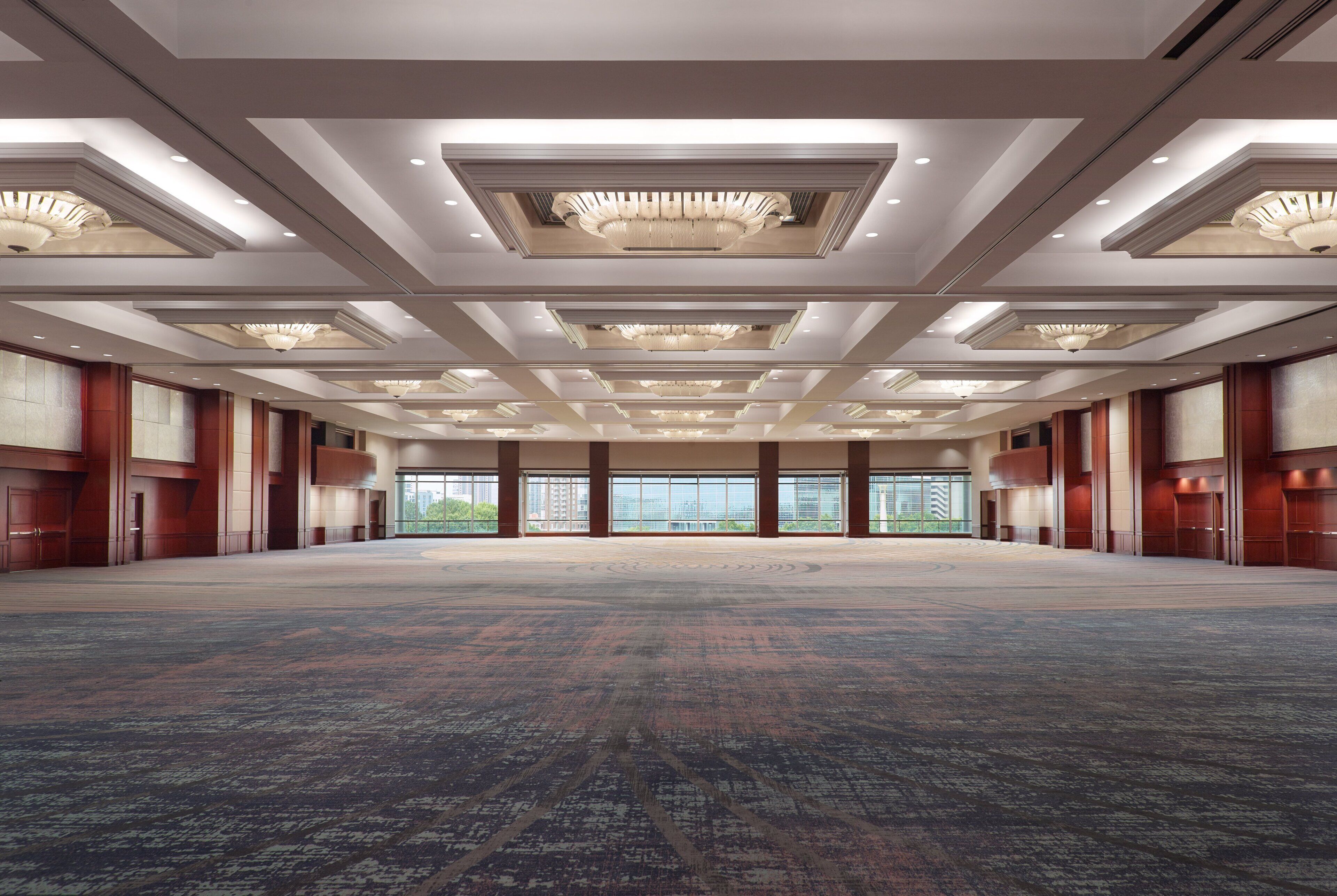 A spacious, well-lit conference room with a patterned carpet, large windows, and a modern ceiling design.