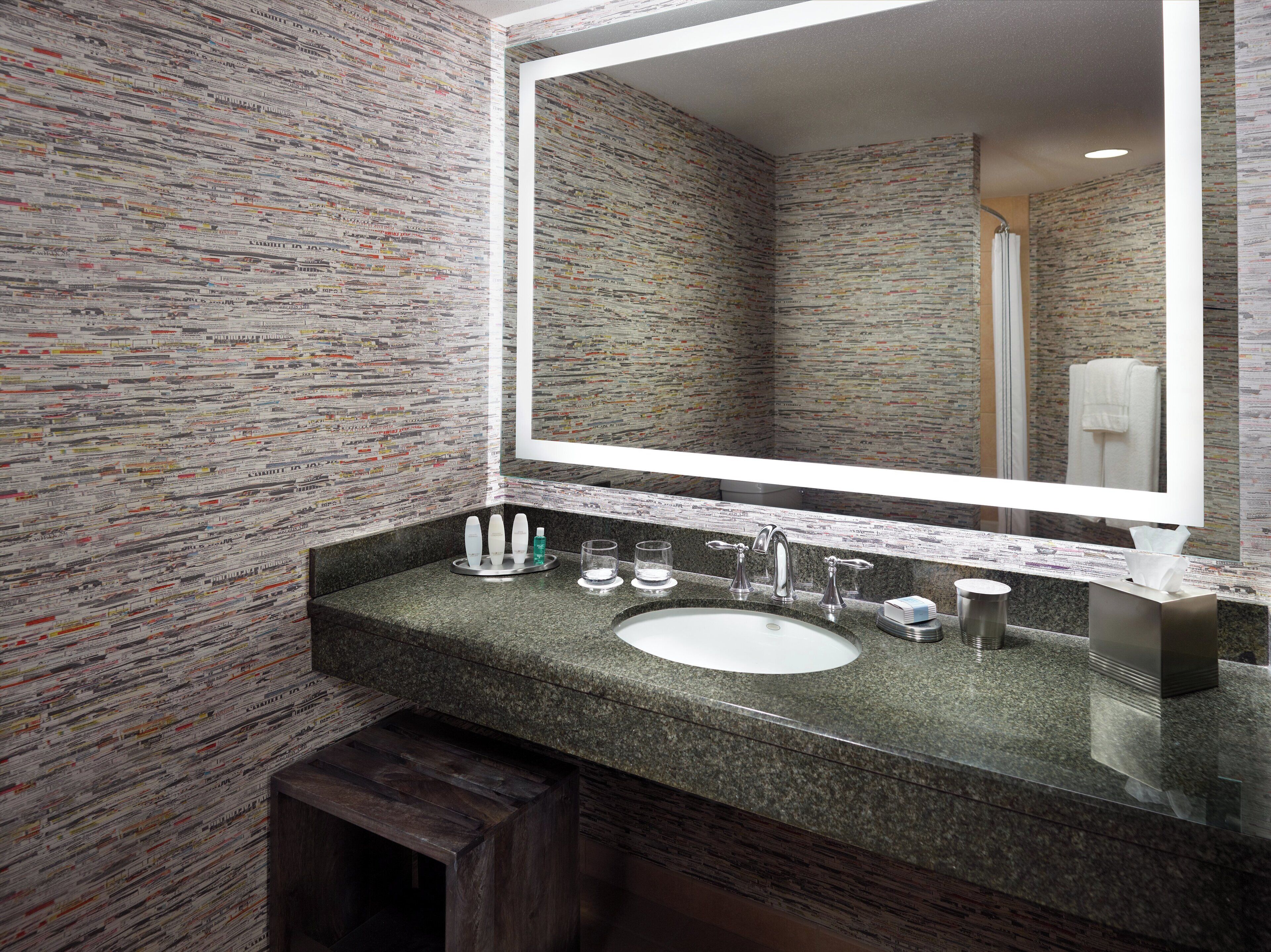 A bathroom with a granite countertop, a sink, a mirror, and a shower visible in the reflection.