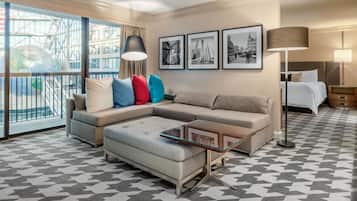 Une chambre d’hôtel moderne avec une grande fenêtre, un canapé, une table basse en verre et un lit.