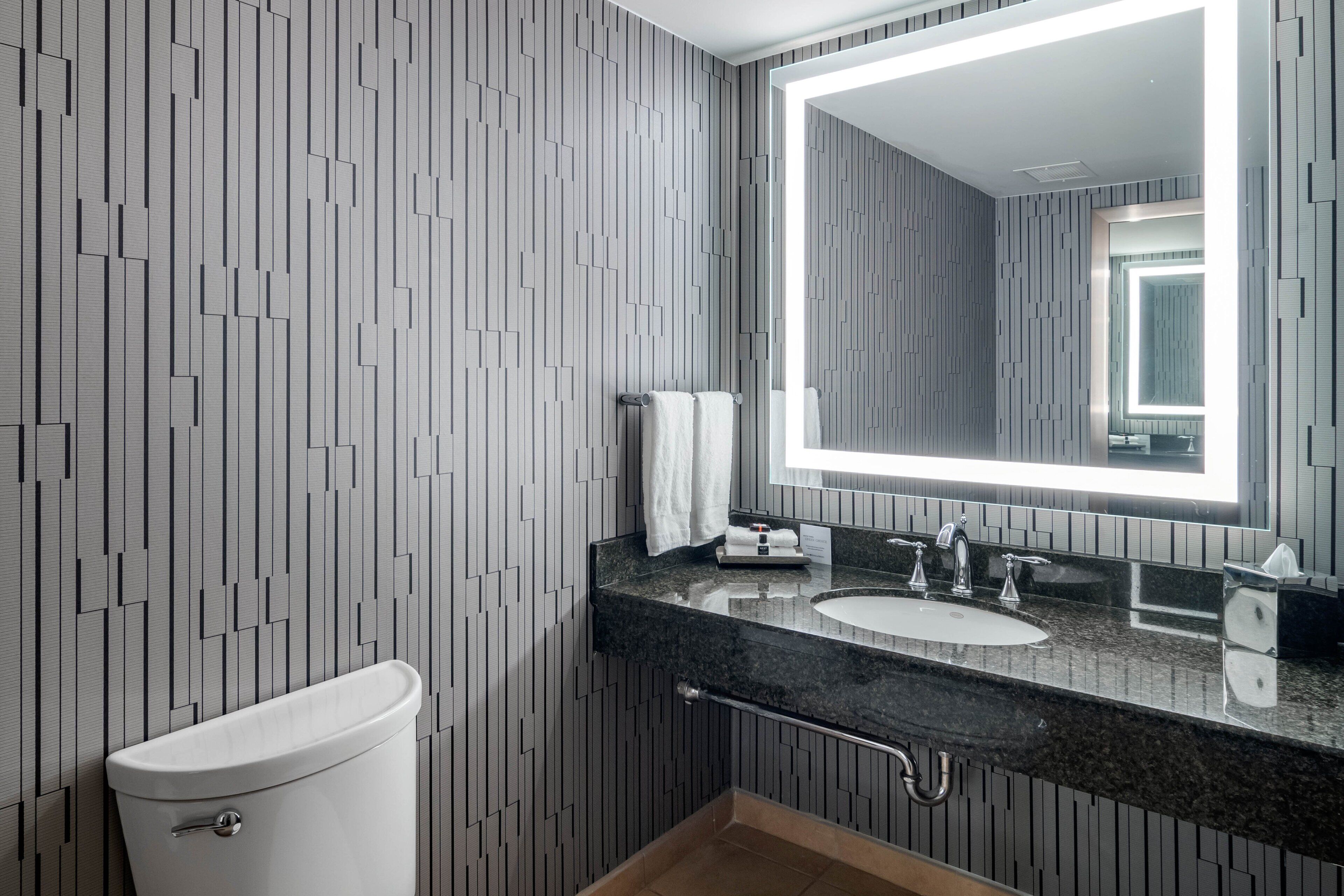 A modern bathroom with a toilet, a sink, and a large mirror.
