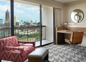 Quarto de hotel com uma janela grande, uma escrivaninha, uma cadeira e um banco.