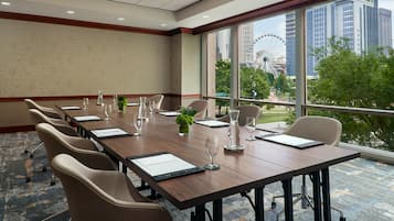 A conference room with a long table, chairs, and a view of a Ferris wheel through large windows.