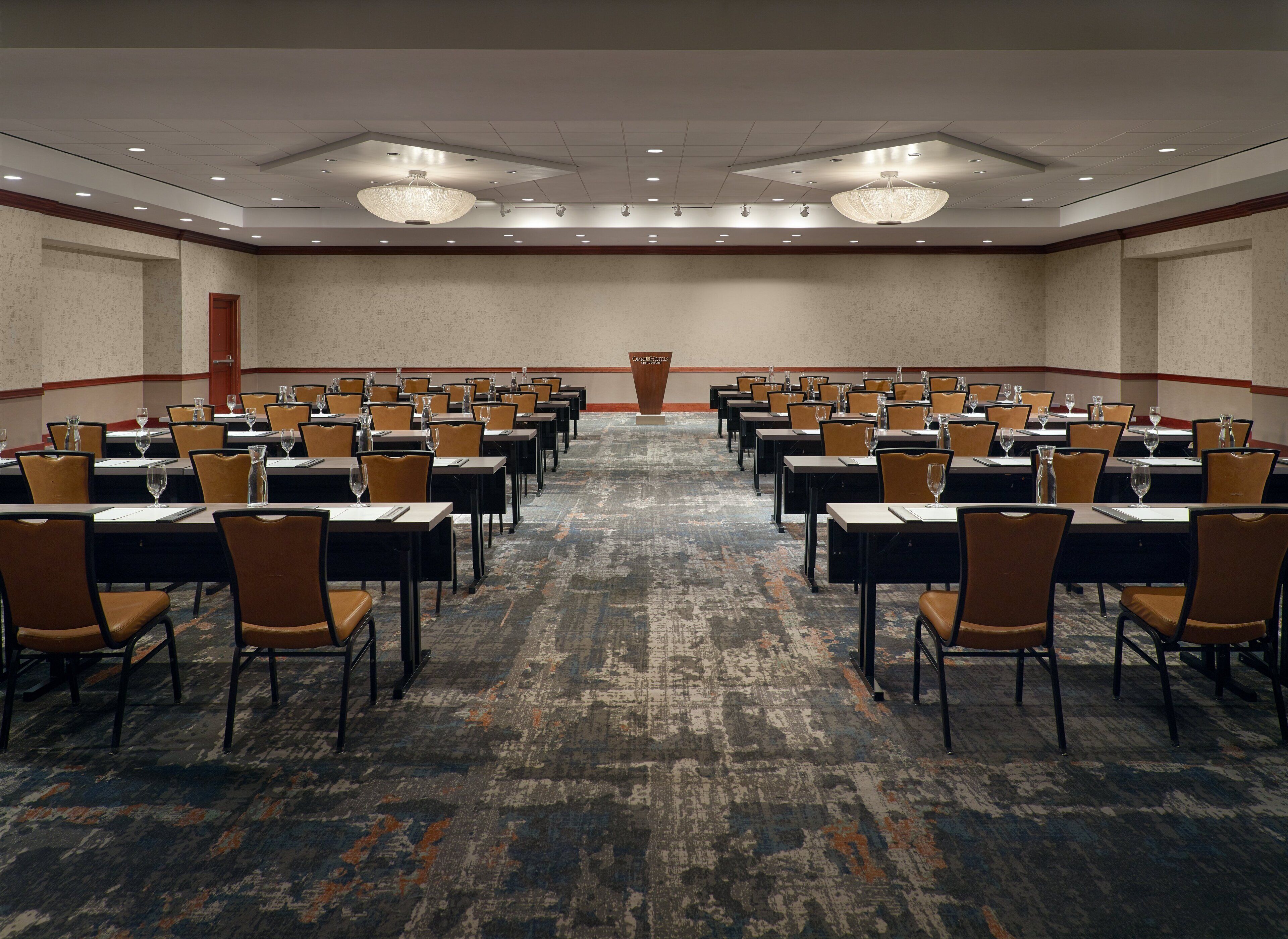 A conference room with rows of tables and chairs, a patterned carpet, and a chandelier.