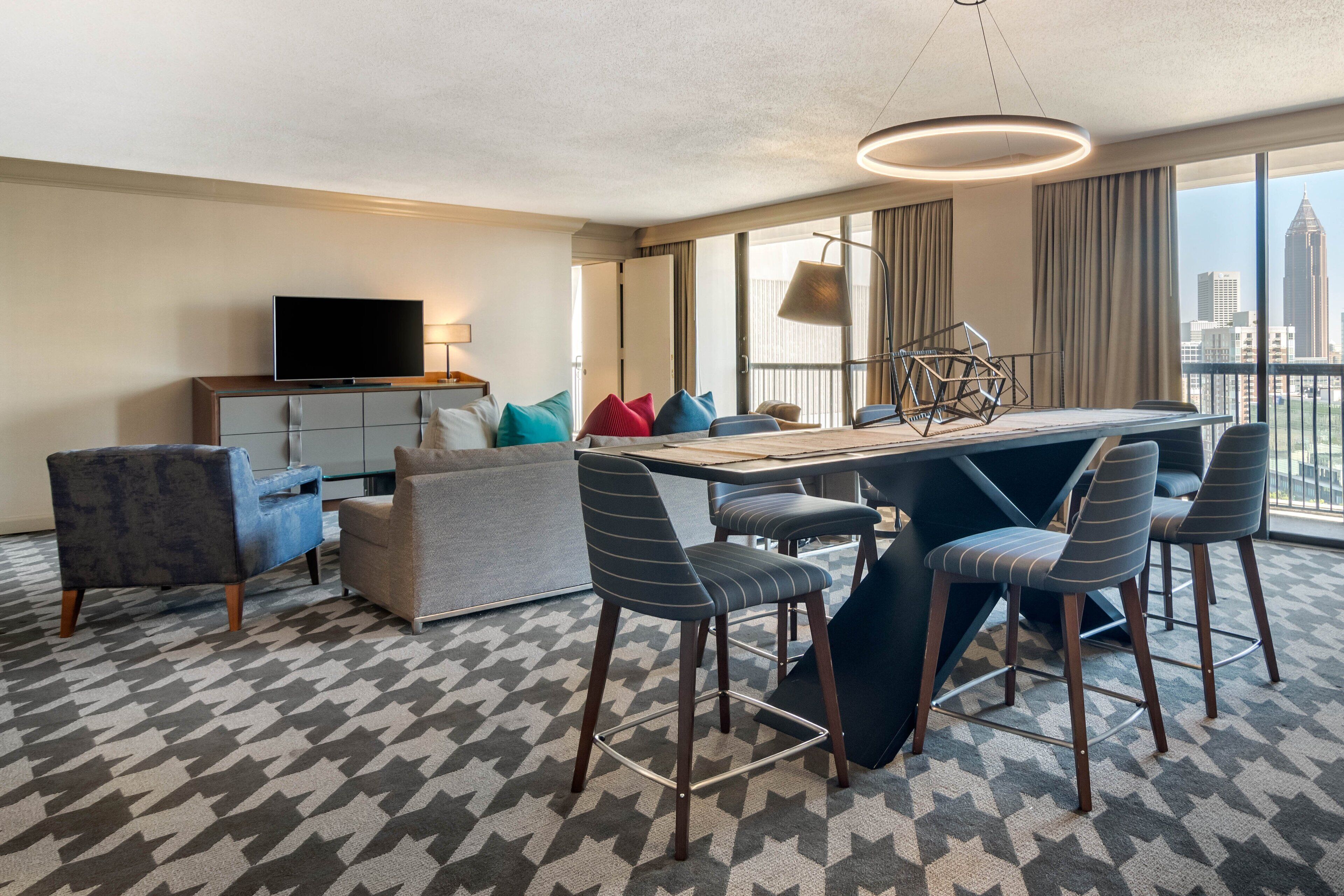 A modern hotel room with a dining area, a TV, and a city view.