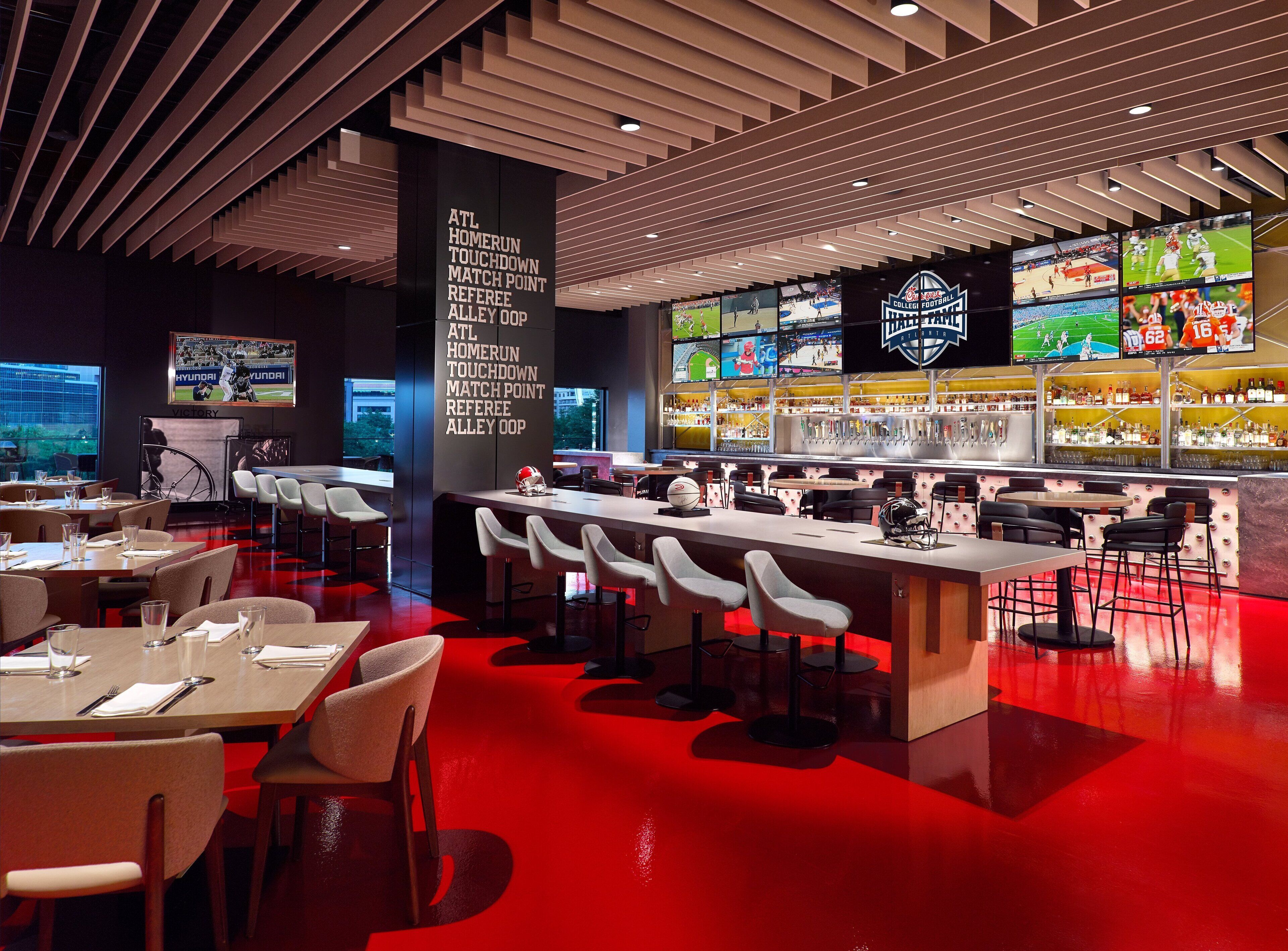 A modern bar area with multiple screens displaying sports events, a bar counter with stools, and a seating area with tables and chairs.