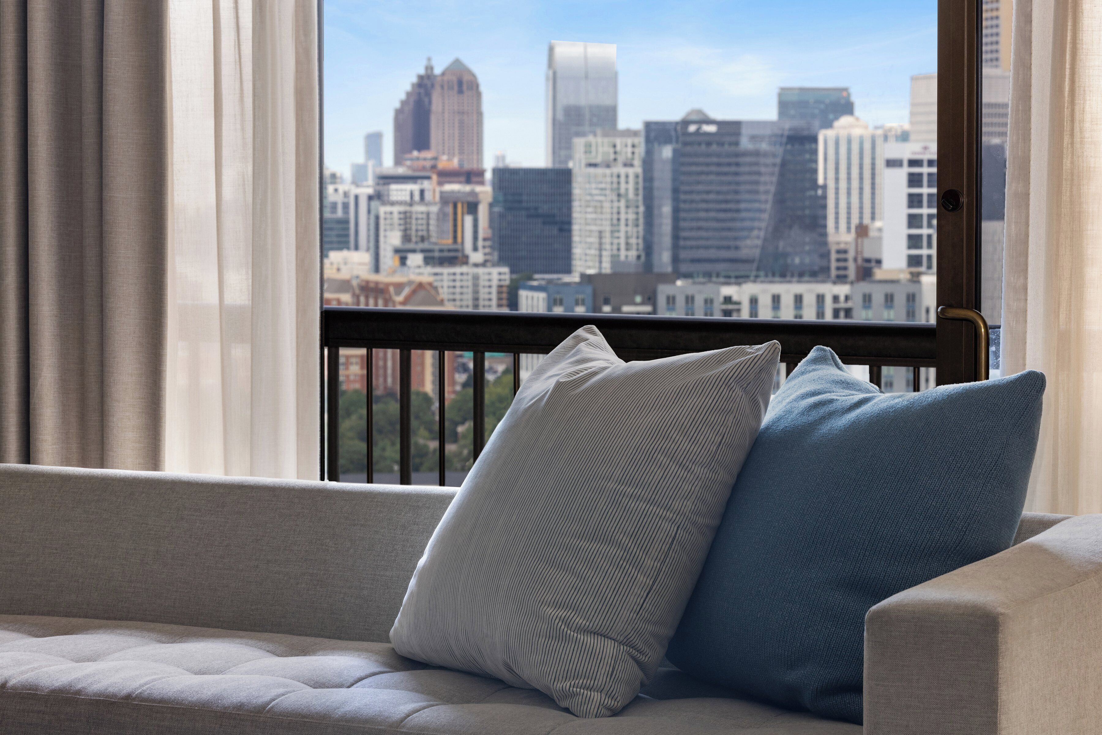 A view of a cityscape through a window with a sofa and two pillows in the foreground.