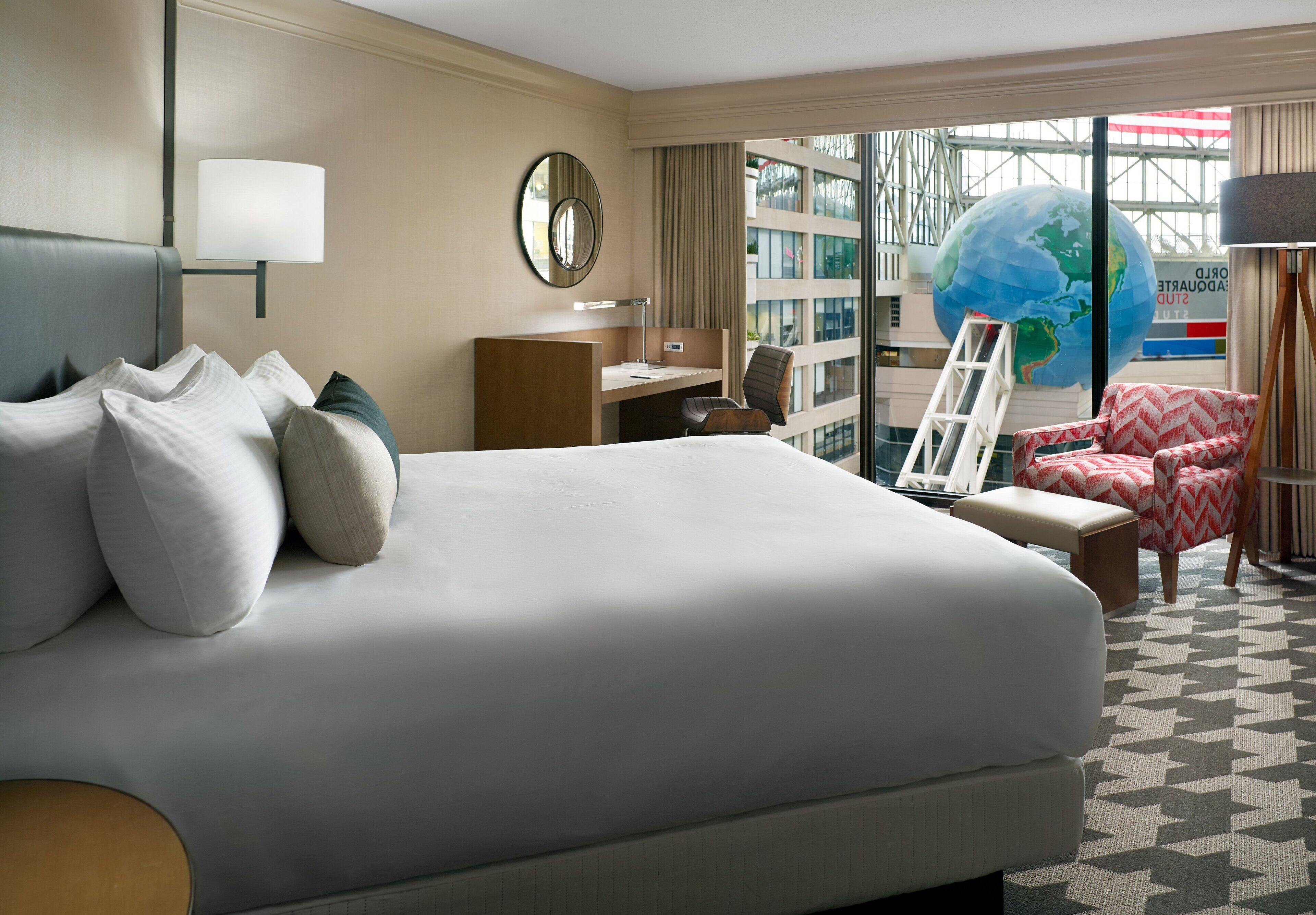 A hotel room with a large bed, a desk, a chair, and a globe.