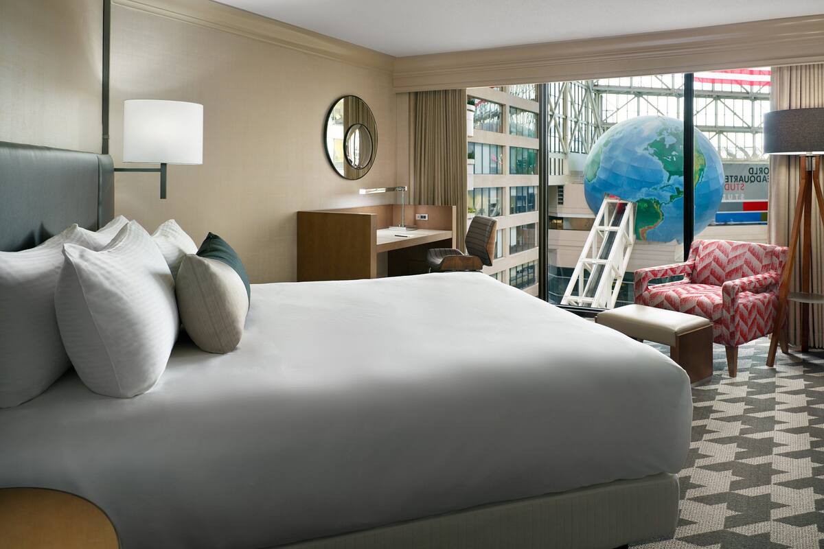 A hotel room with a large bed, a desk, a chair, and a globe.