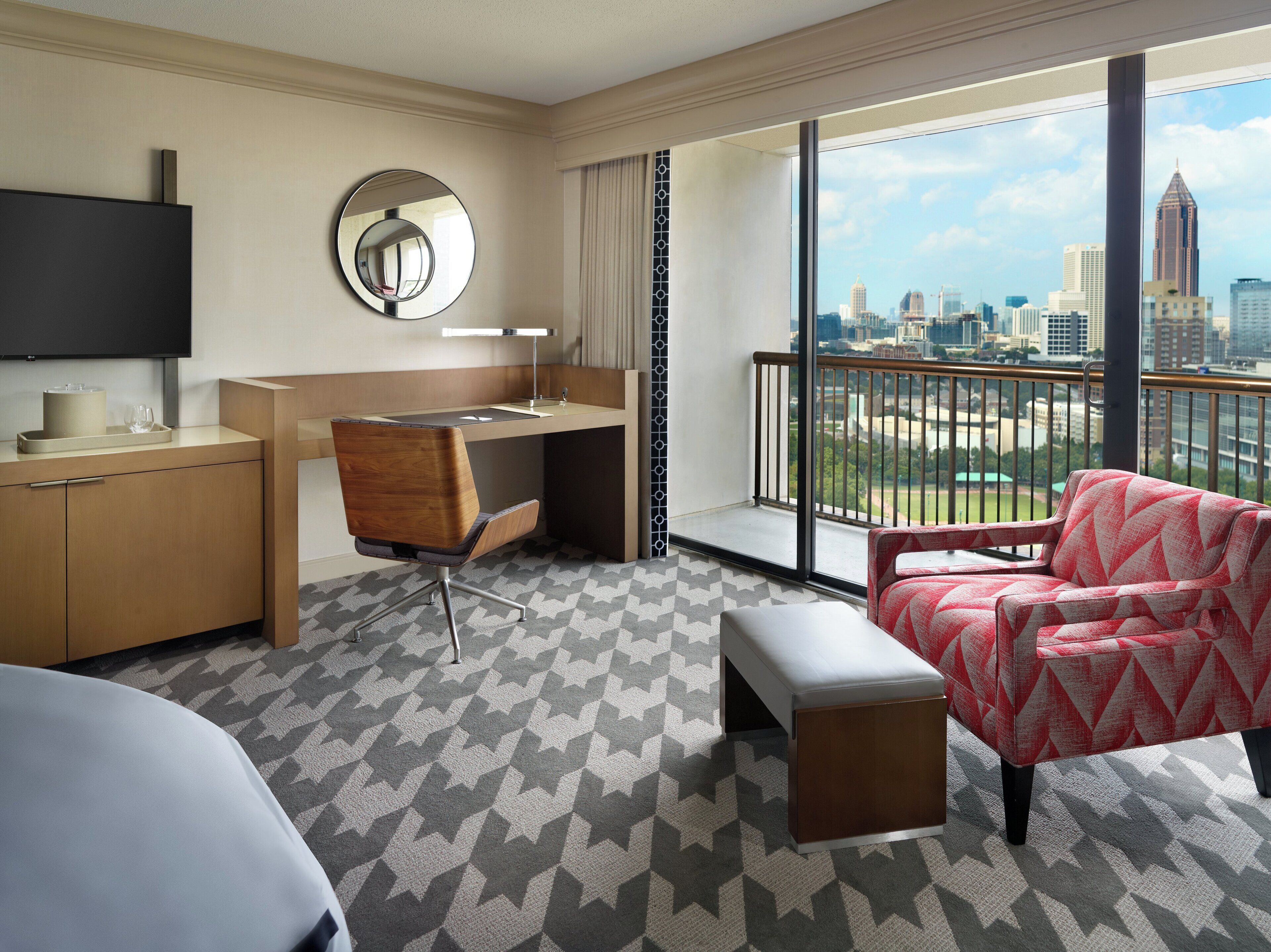 A hotel room with a desk, chair, and a large window offering a city view.
