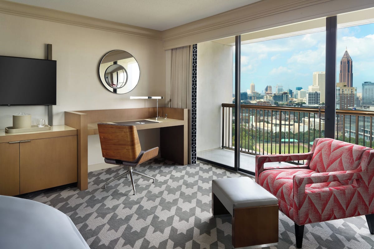 A hotel room with a desk, chair, and a large window offering a city view.