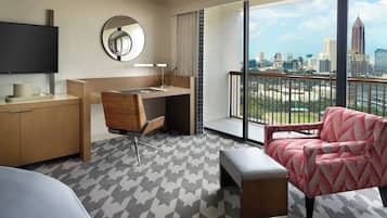 A hotel room with a desk, chair, and a large window offering a city view.