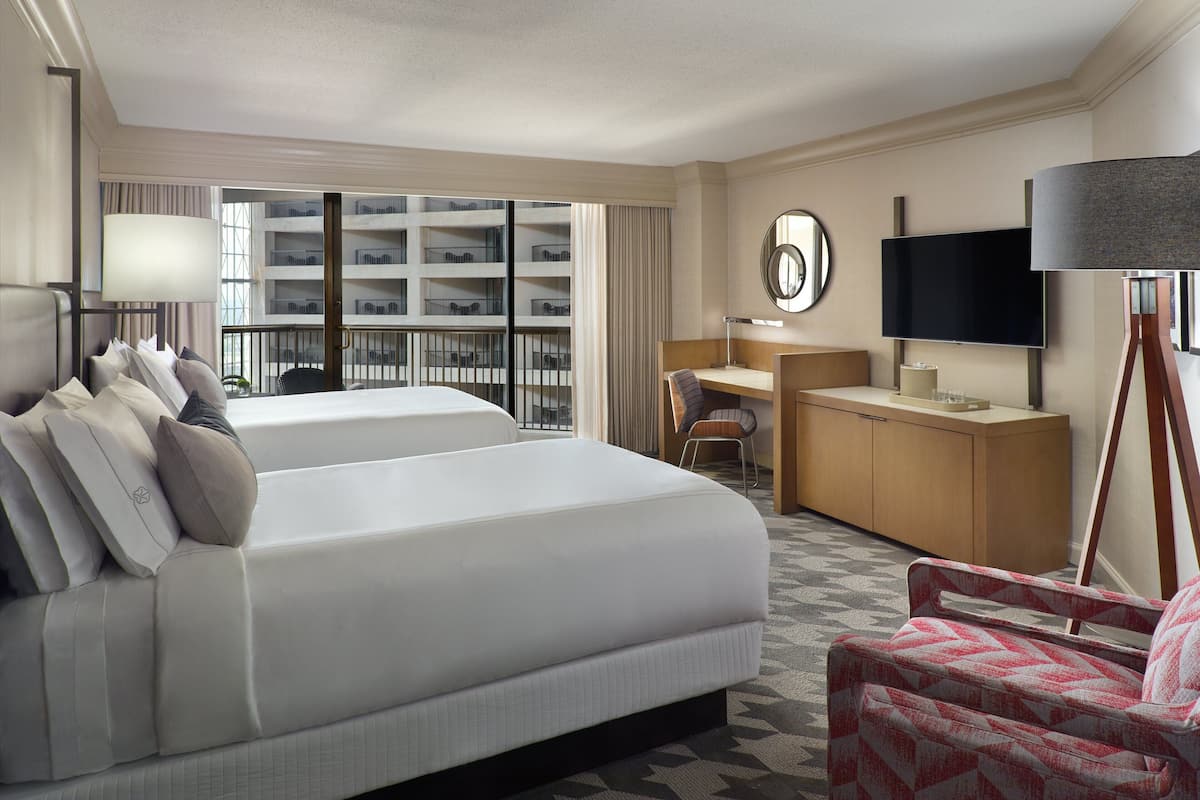 A hotel room with a large bed, a desk, a chair, a TV, and a view of the building's interior.