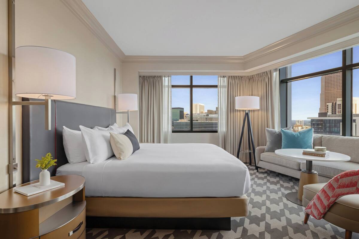 A hotel room with a large bed, a sofa, a small table, and a view of the city.