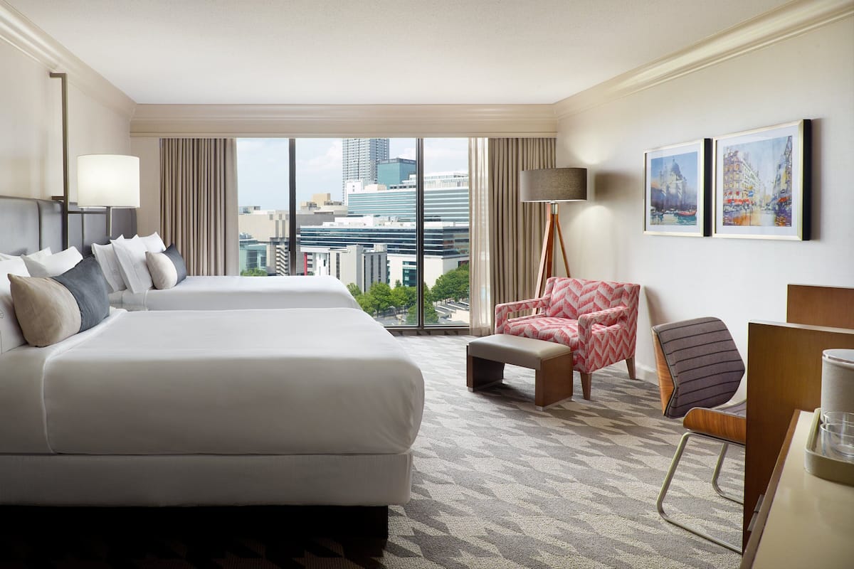 A hotel room with a large bed, a desk, a chair, and a view of the cityscape.