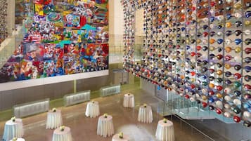 A lobby with a large Penley artwork, a wall of helmets, and round tables with flowers.
