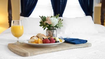 Um café da manhã bem arrumado sobre a cama, com um copo de suco de laranja, um prato de croissants, morangos, amoras e um pequeno vaso com flores.