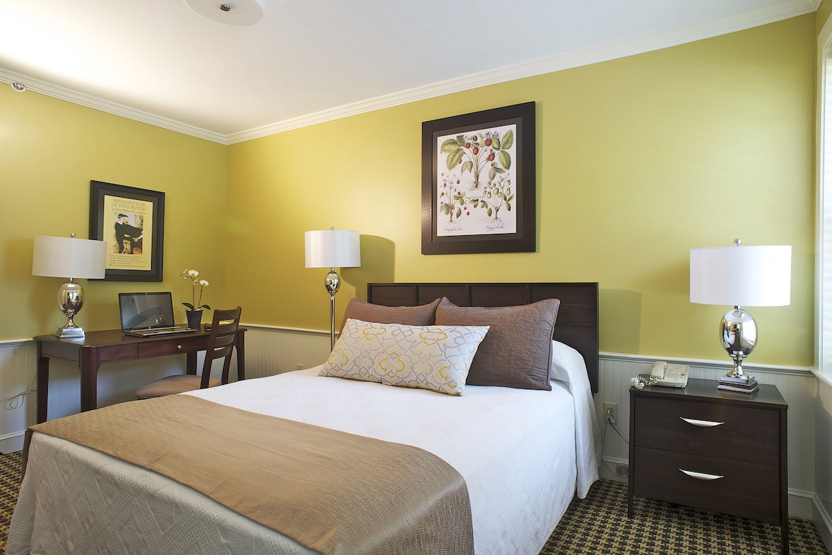 Quarto de hotel com cama, duas mesas de cabeceira, escrivaninha e uma cadeira.