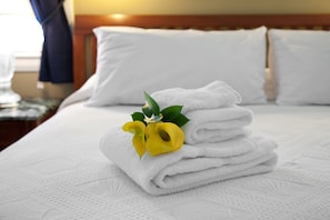 A neatly made bed with white linens and a yellow flower arrangement.