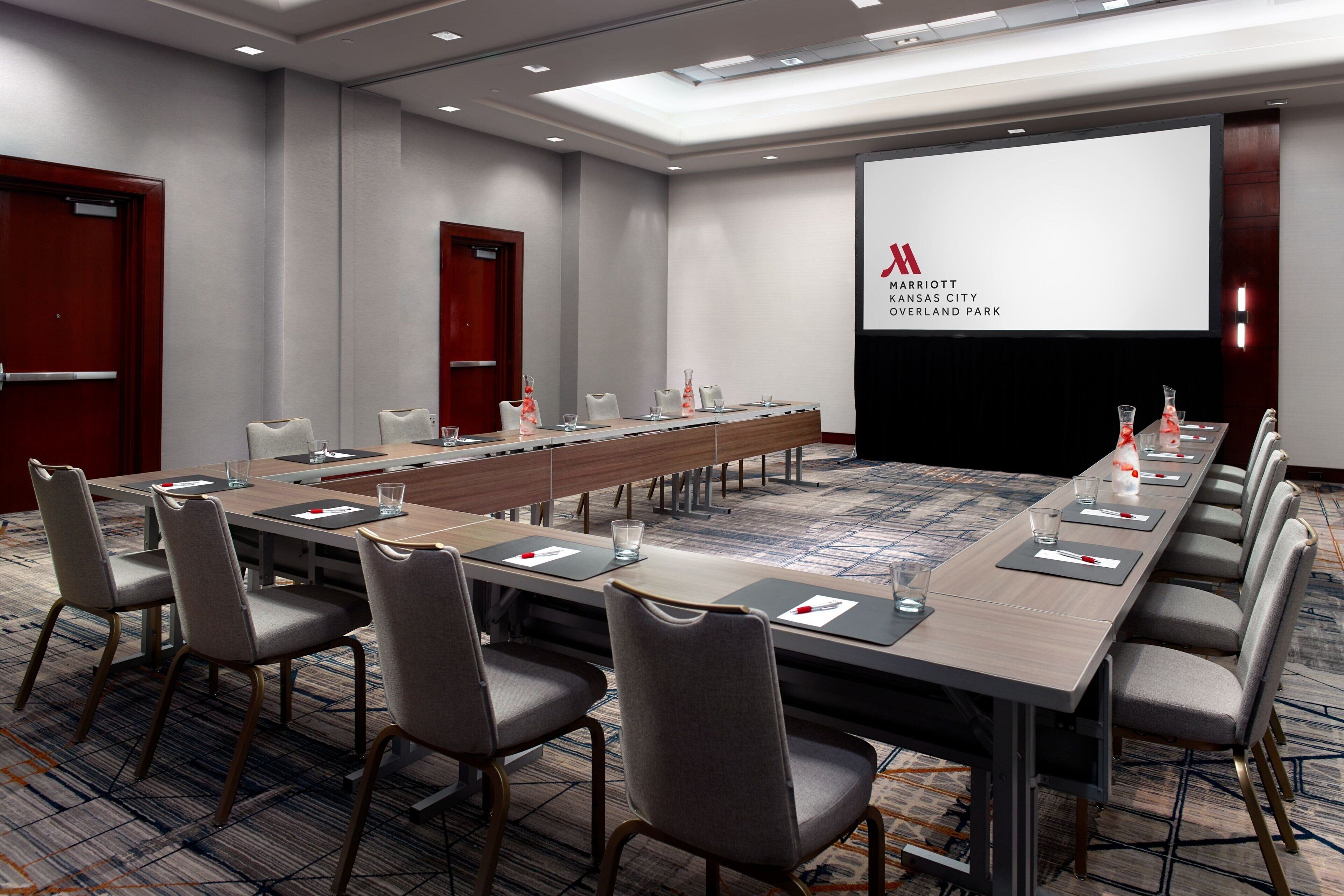 A conference room with a long table, multiple chairs, and a presentation screen.