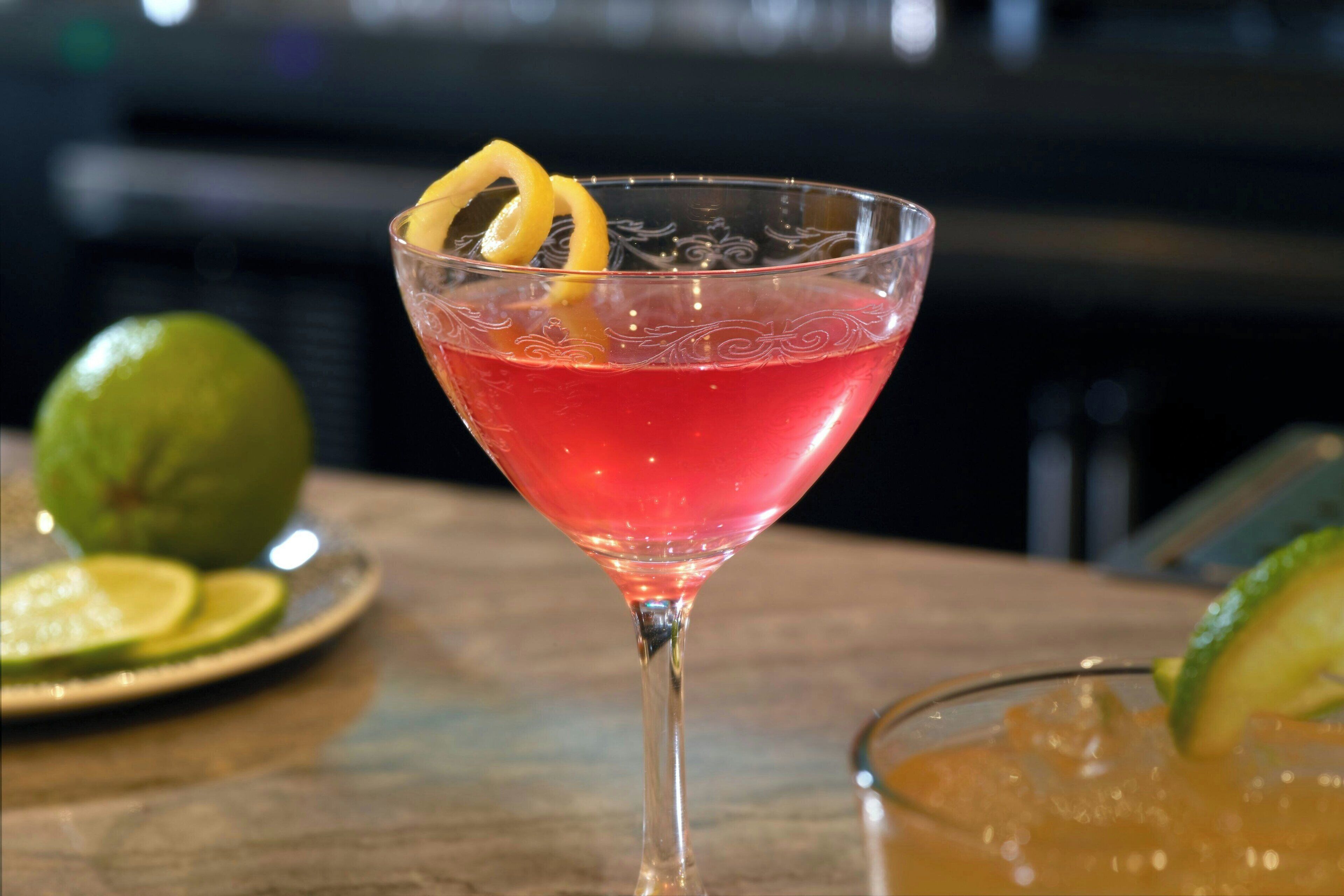 Un cocktail servi dans un verre à martini, garni d’une tranche de citron vert, posé sur une table en bois.