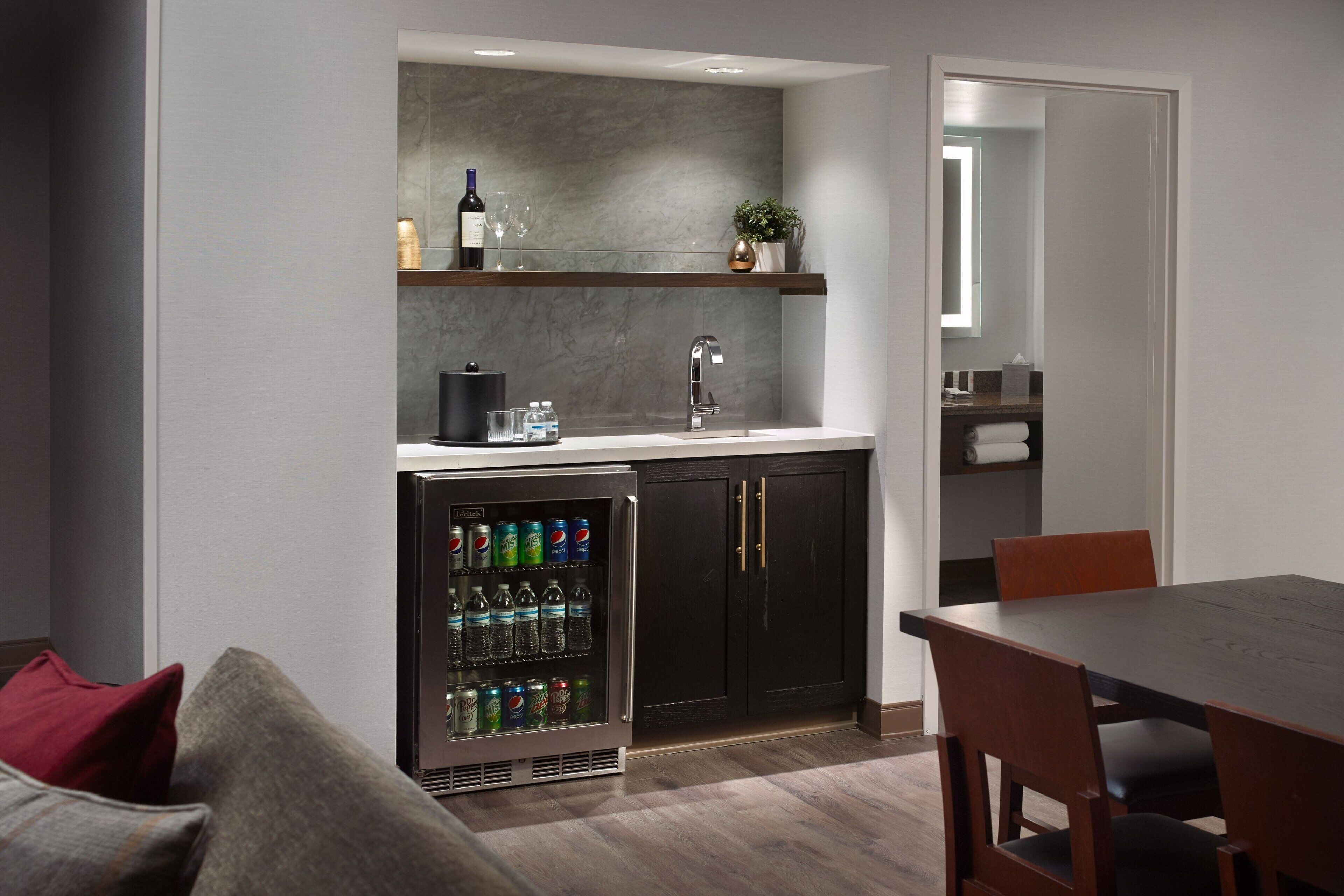 A modern kitchen with dark cabinetry, a built-in wine cooler, and a refrigerator stocked with beverages.