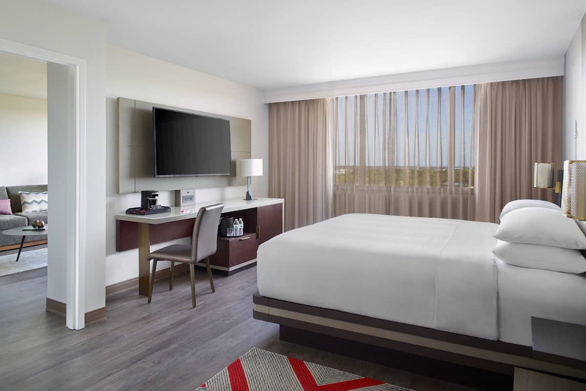 Ein Hotelzimmer mit einem großen Bett, einem Schreibtisch mit Computer, einem Fernseher und Blick auf die Stadt durch das Fenster.