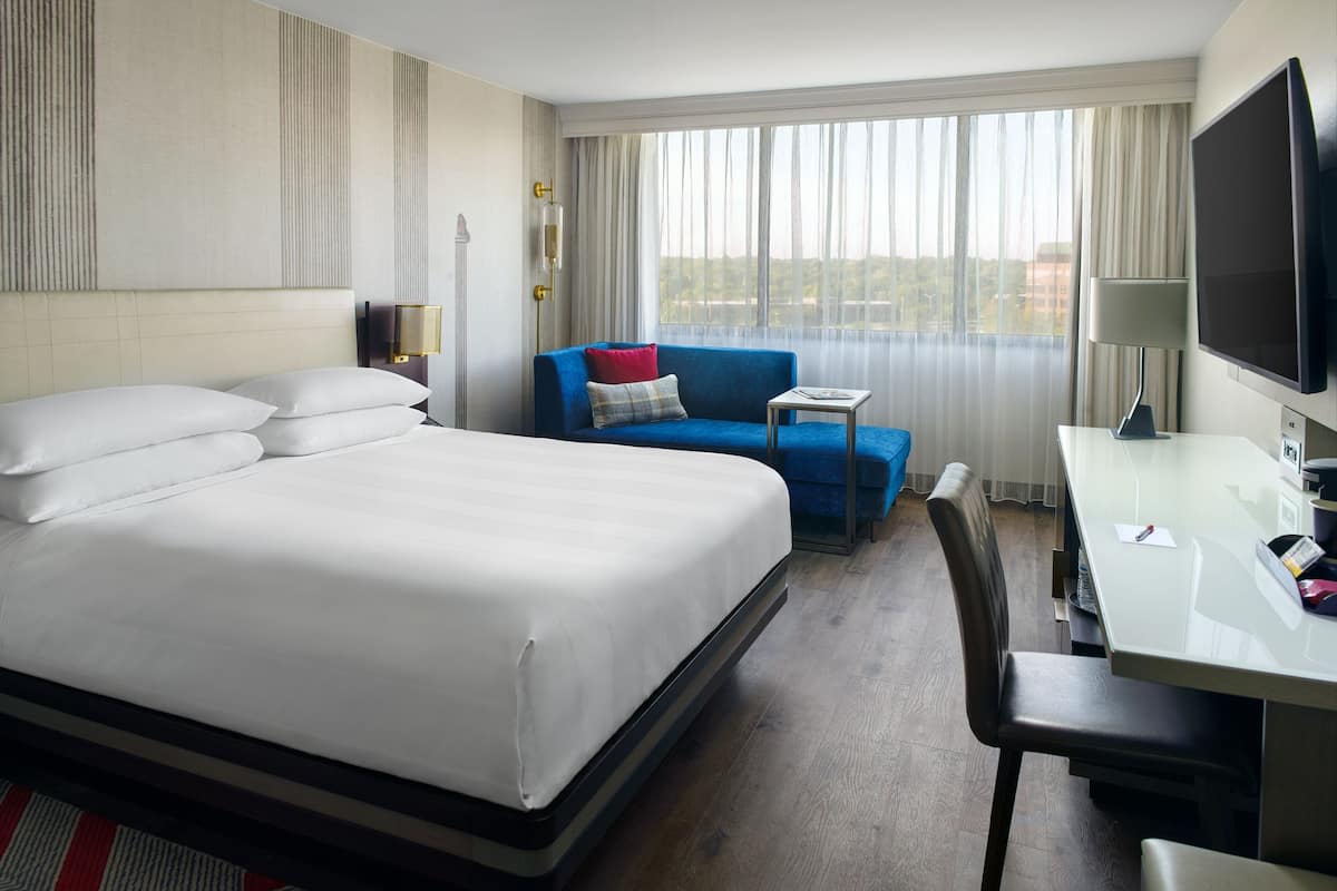 Ein Hotelzimmer mit einem großen Bett, einem Schreibtisch mit Stuhl, einem blauen Sofa und einem Fernseher.