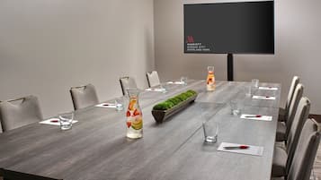 Un salón de conferencias con una larga mesa, sillas, una pantalla de televisión y una planta pequeña sobre la mesa.