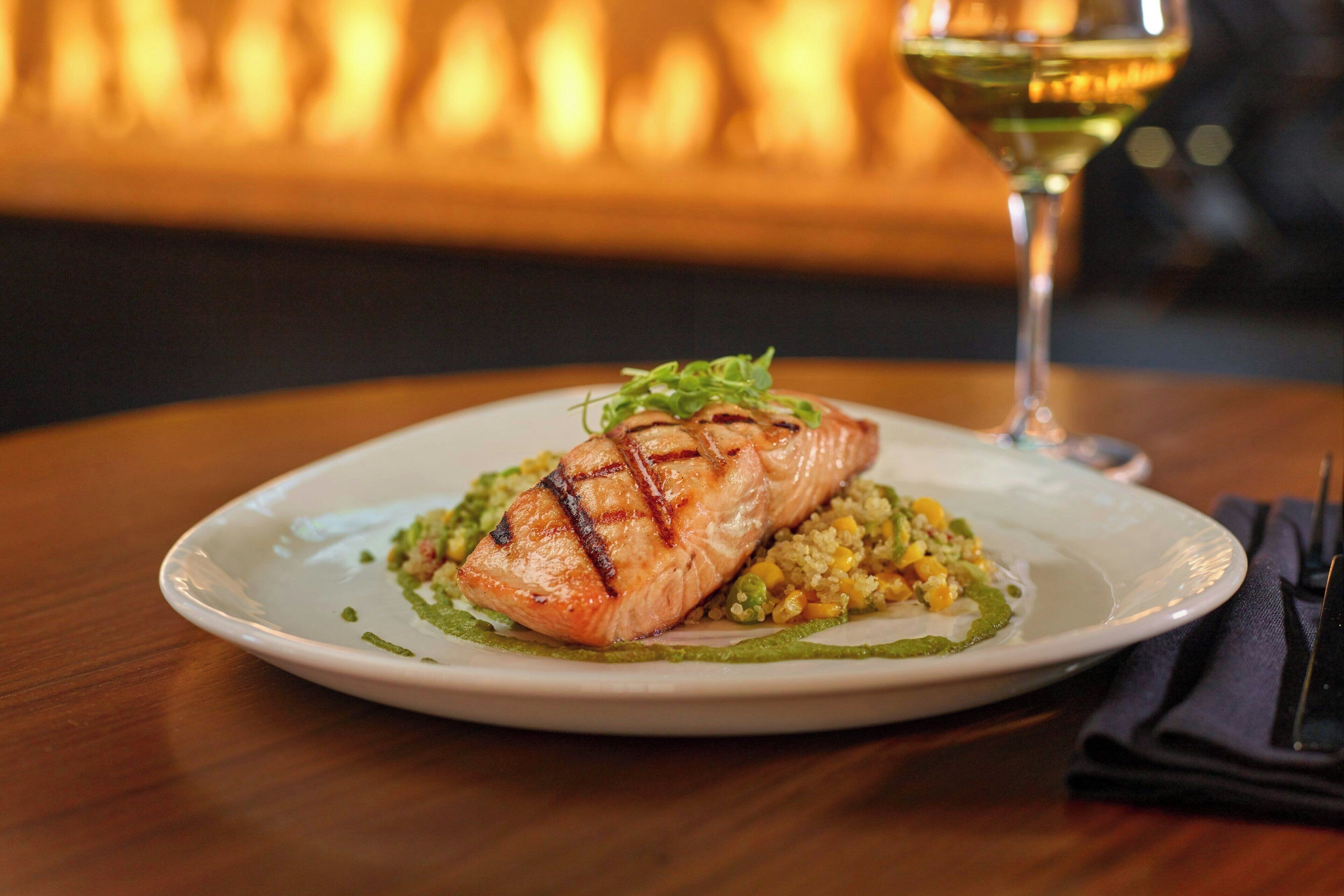 A plate of grilled salmon with a side of vegetables and a glass of white wine on a wooden table.