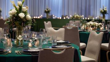 A formal dining setting with tables set for multiple guests, featuring elegant tablecloths, glassware, and floral centerpieces.