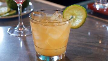 A glass of a light-colored beverage with ice cubes and a lime slice garnish, placed on a bar counter.