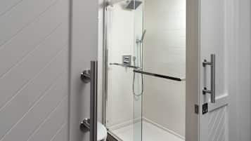A modern bathroom with a glass shower enclosure, white tiled walls, and a visible toilet.