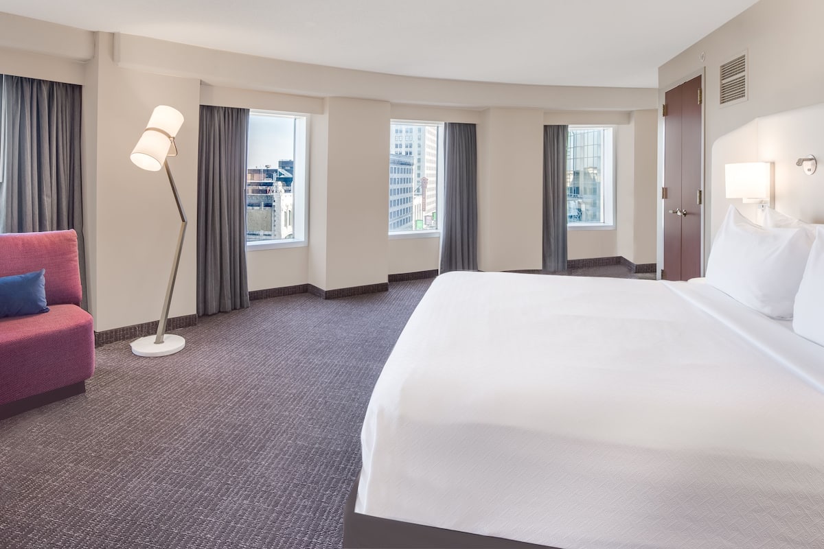 A hotel room with a large bed, a desk, a chair, and a floor lamp.