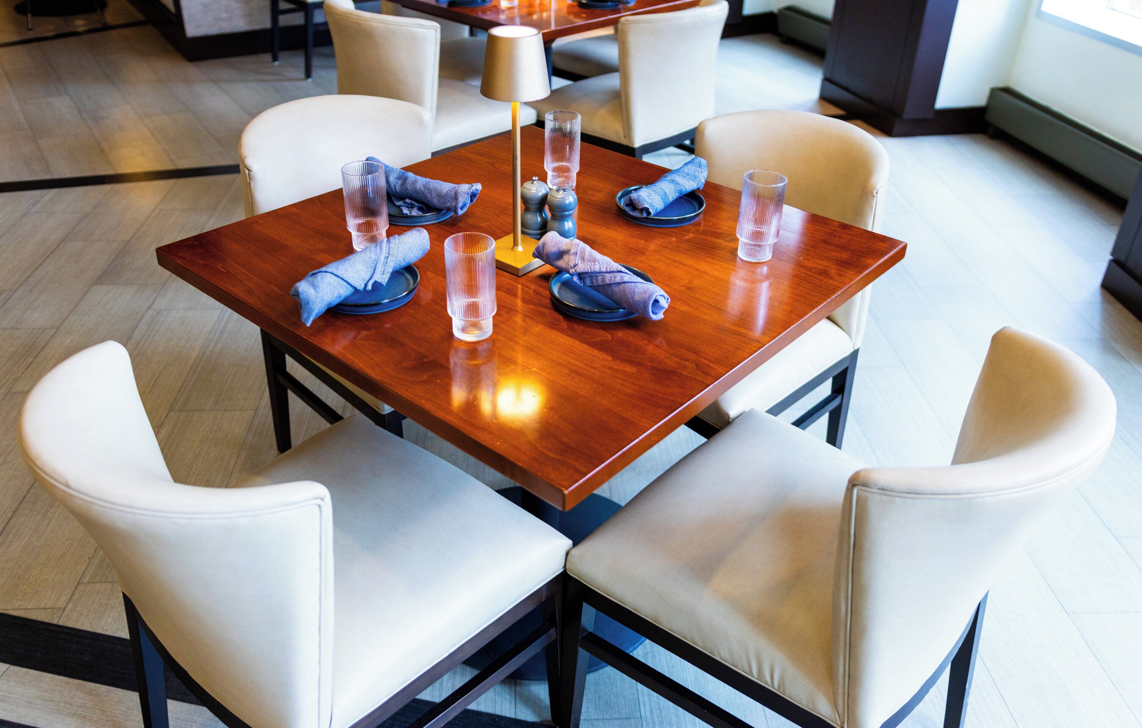 Un comedor con una mesa de madera, sillas blancas con acolchado y servilletas azules dobladas con esmero.
