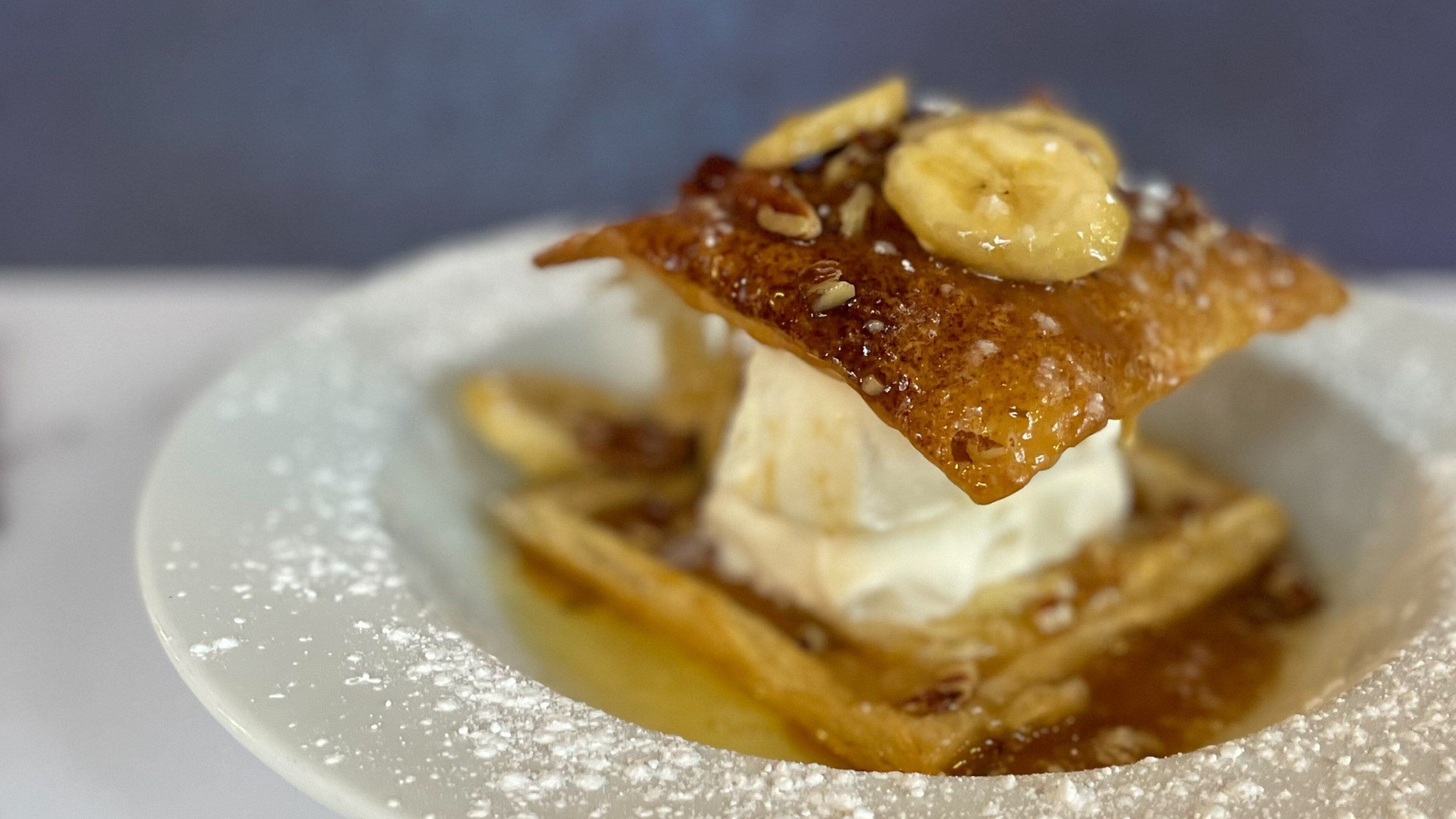 A dessert with a banana slice on top, served on a white plate with powdered sugar.