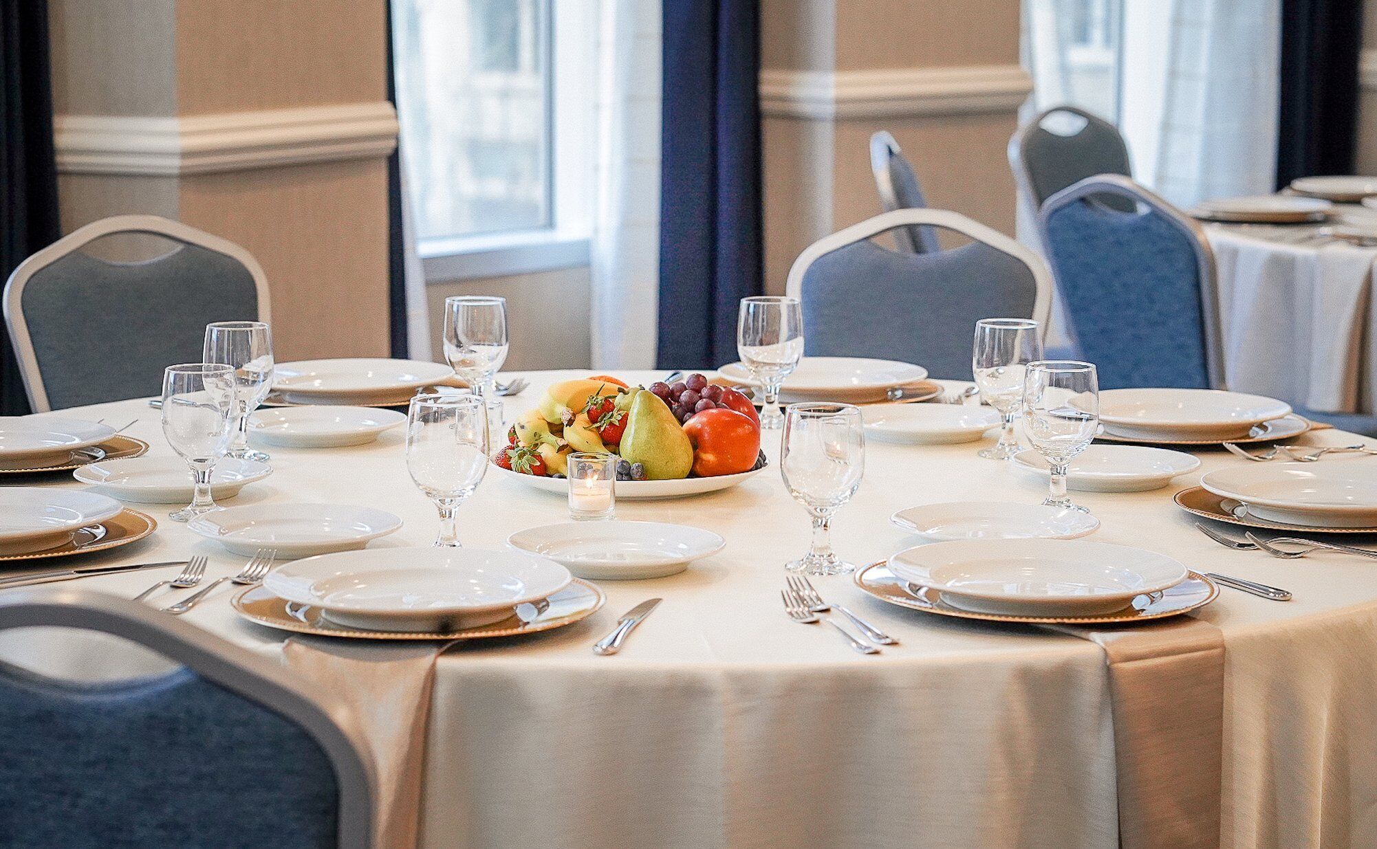 A dining table set with plates, glasses, and cutlery, centered with a fruit bowl.