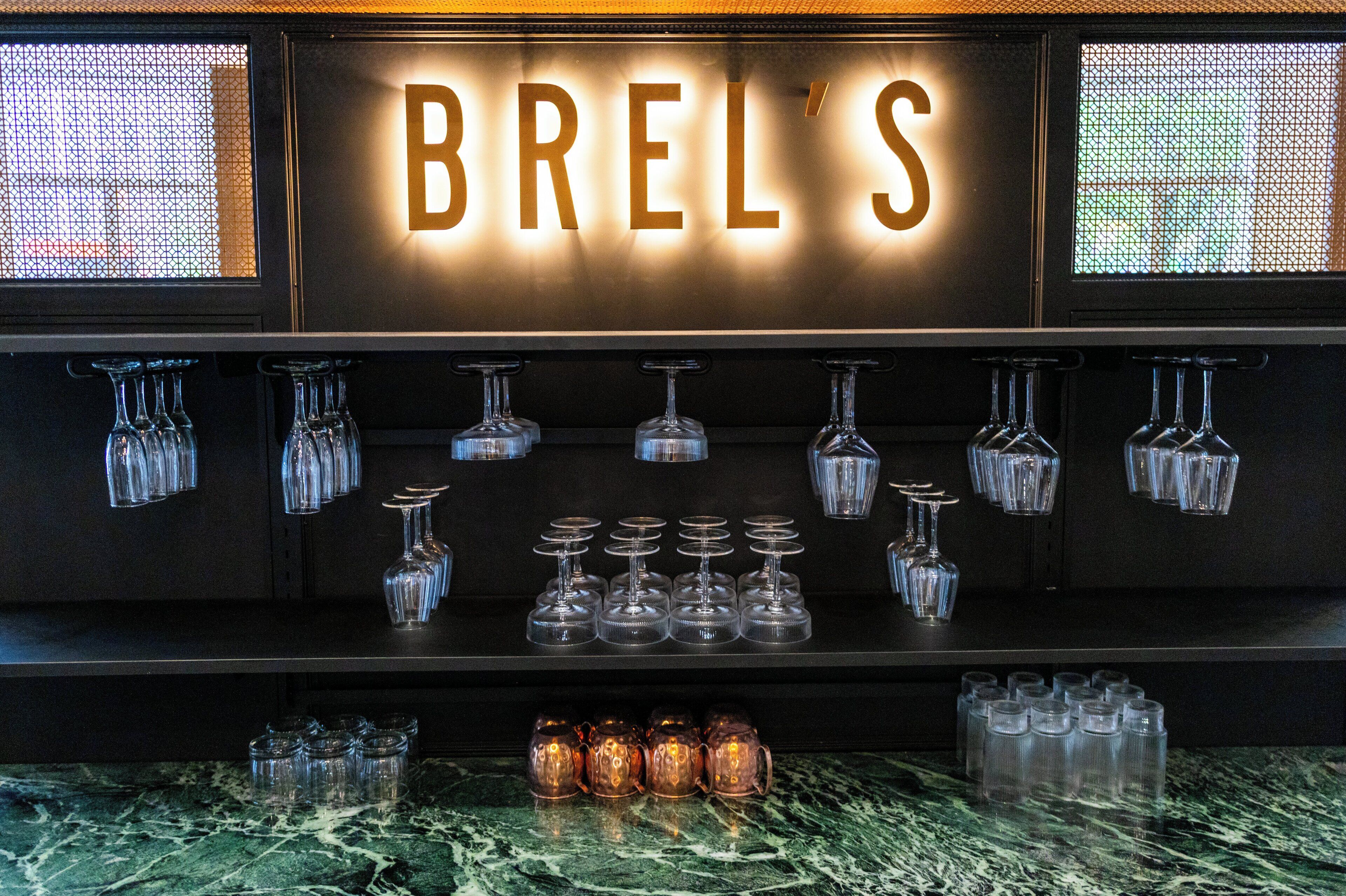 Una zona de bar con un letrero que dice "BRELS" y diferentes vasos exhibidos en estanterías.