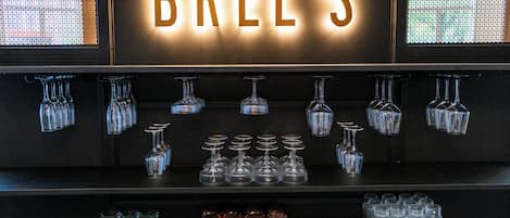 Una zona de bar con un letrero que dice "BRELS" y diferentes vasos exhibidos en estanterías.