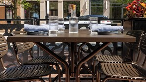 Un área de estar al aire libre con una mesa dispuesta para dos personas, con sillas de metal y una mesa de vidrio.